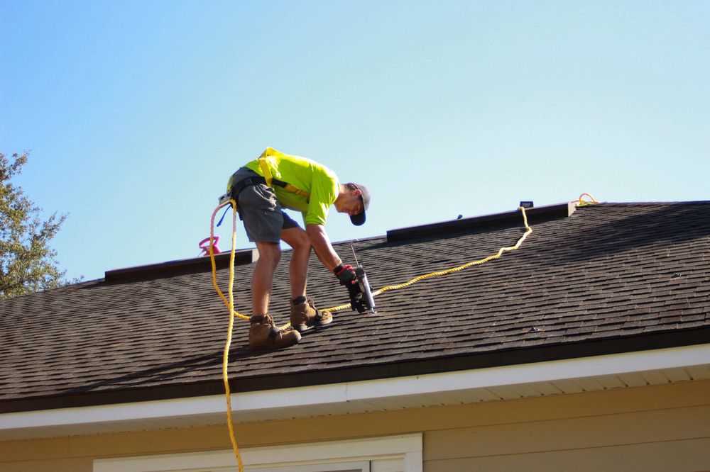 Contractor In Safety Harness Using Caulk Gun On Roof