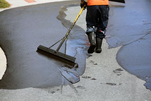 Top 10 Tips For DIY Driveway Sealing Man Spreading Sealant On Driveway with Driveway Coater Brush.