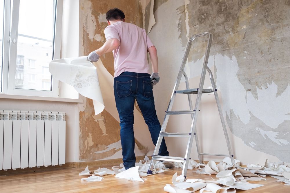 Man removing wallpaper from wall next to window
