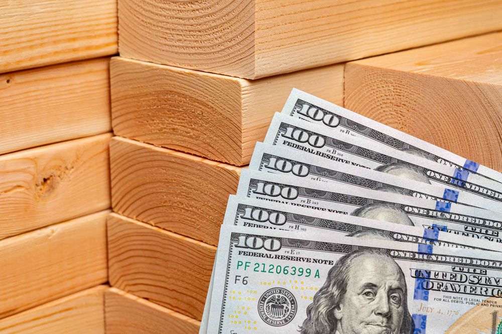 Stacks of 2x4s behind six $100 bills in United States currency.