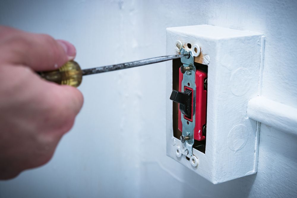 Homeowner Adjusting Light Switch Assembly Screw With Screwdriver.
