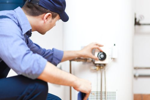 11 Tips For Buying a New Water Heater HVAC pro kneeling to adjust temperature dial on newly installed water heater